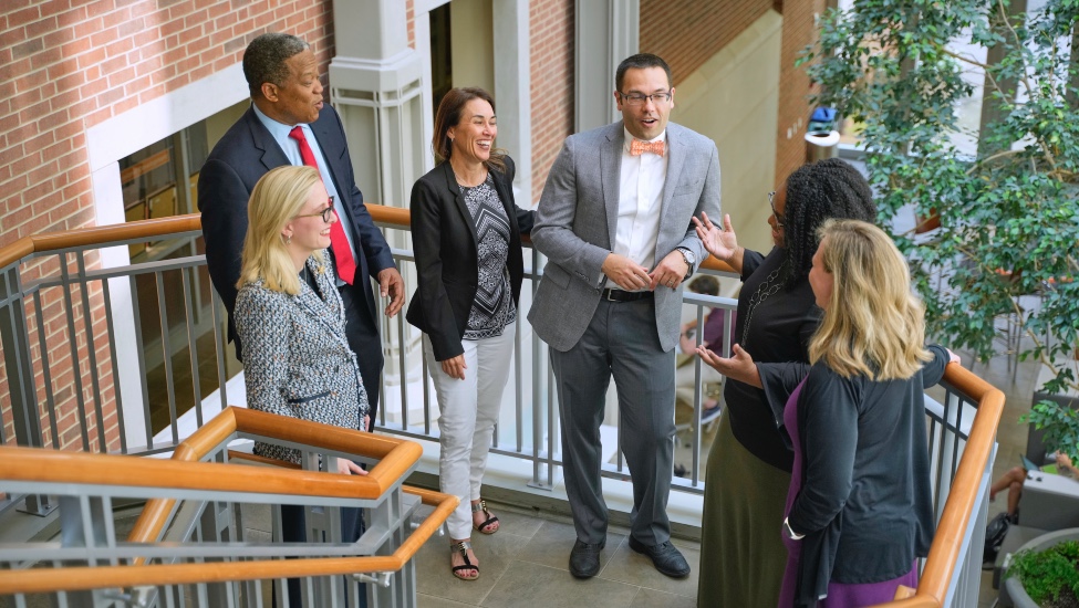 Multicultural male and female graduate students talk while standing on open staircase landing