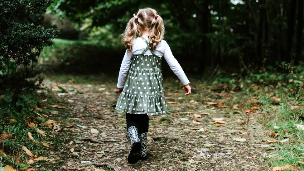 Young child with pigtails walks on path into woods