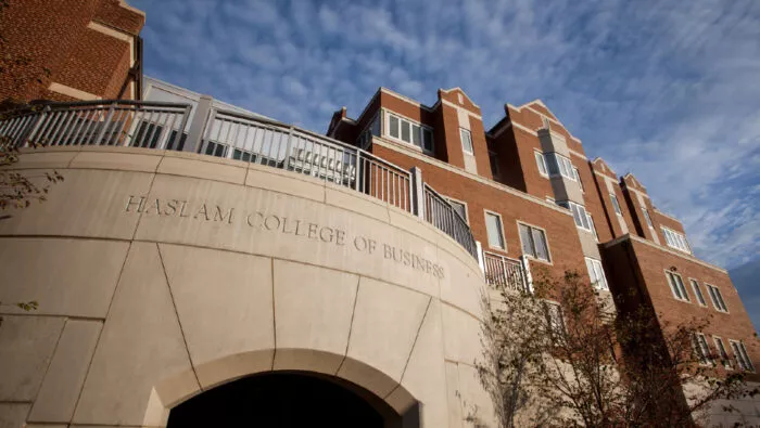 View of Haslam College of Business building from the south sidewalk, showing its side balcony with the sky and thin white clouds above