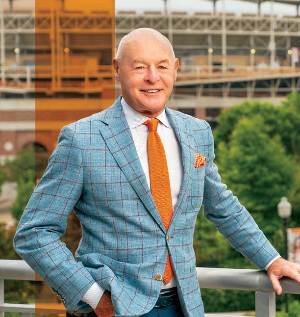 Larry Pratt stands in front of with Neyland Stadium with a transparent orange stripe behind his shoulder. He is smiling at the camera.