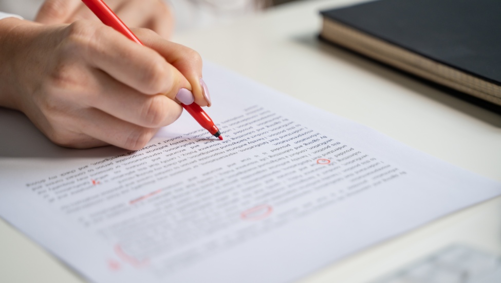 Close-up of a hand holding a red pen, making edits on a printed document