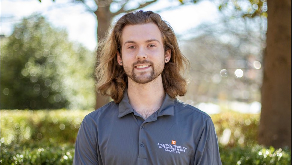 Outdoor head and shoulders shot of Brennan Lessard wearing a gray polo shirt with the UT Anderson Center for Entrepreneurship and Innovation logo