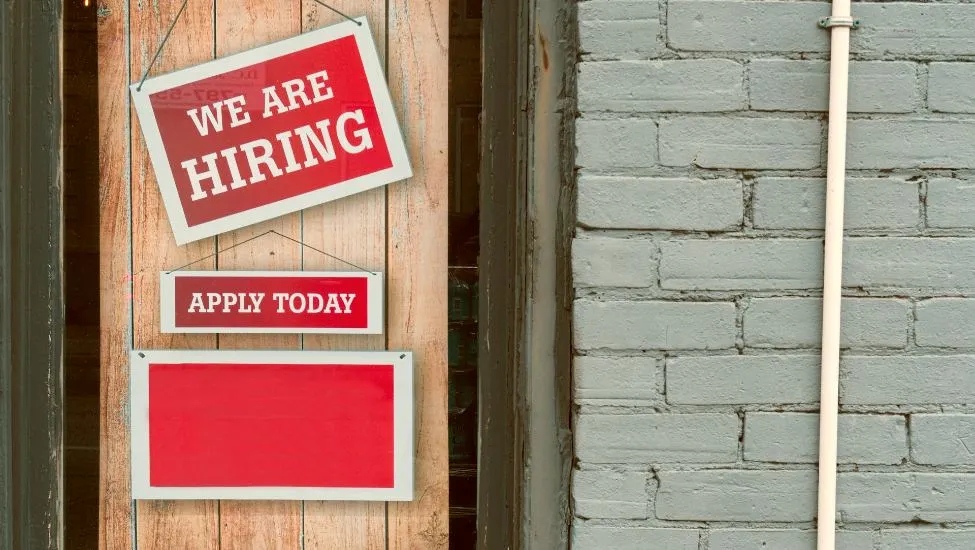 Signage hanging on a door reads "We're Hiring, Apply Today"
