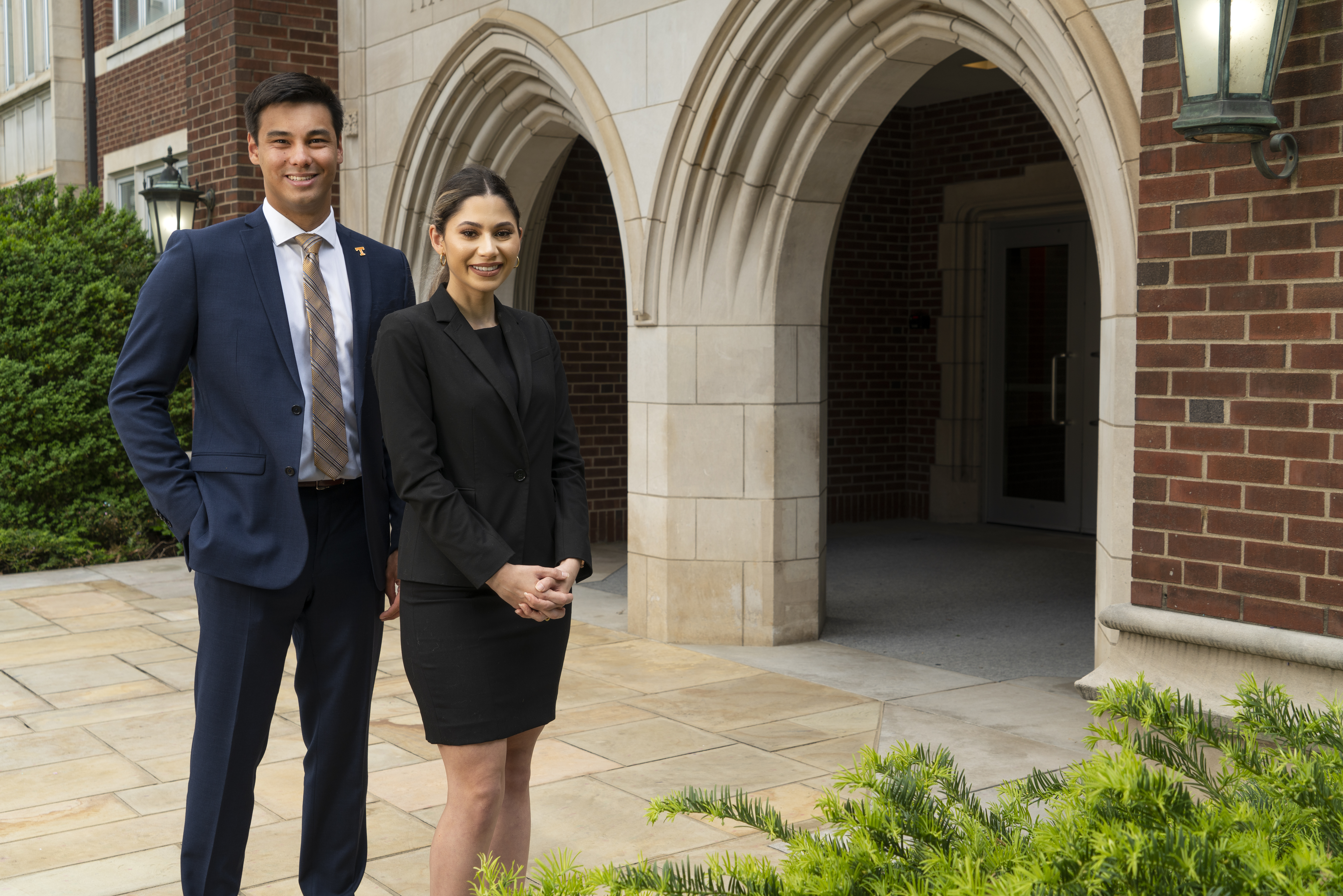 Two professionally dressed graduate students (male and female) smiling at the camera while posing in front of the Haslam Business Building arches.