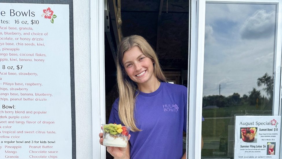 Kendel Locke in the window of the Hula Bowls shed, holding a smoothie and smiling