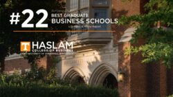 The words "#22 Among Publics Best Graduate Business Schools - U.S. News and World Report" printed in white above a thin orange bar with "Haslam College of Business, University of Tennessee, Knoxville" printed below them are superimposed on a late-afternoon photo of entrance to the Haslam Business Building, taken from under the shade of trees.