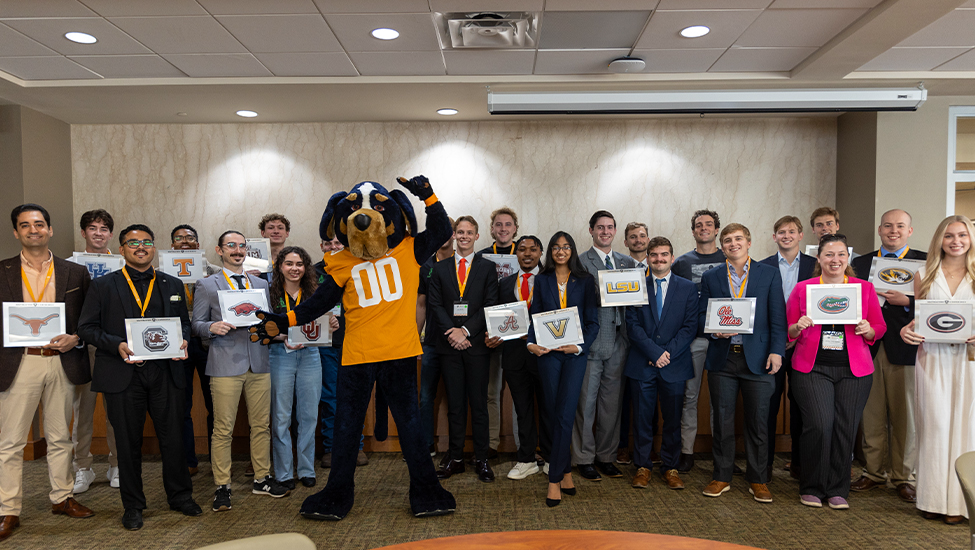 Students participating in the 2024 SEC Pitch competition hold signs featuring their respective university logo and pose with Smokey, UT's mascot.