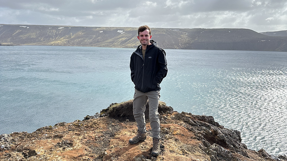 Kaelan Cook stands on a cliffside over a body of water in Iceland.