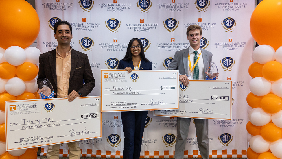 2024 SEC Pitch Competition winners pose with large novelty checks in front of an Anderson Center and SEC step-and-repeat.