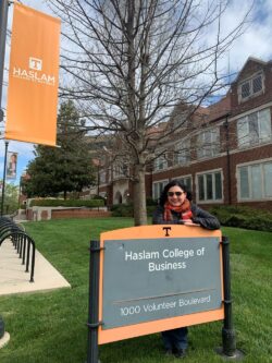 In a jacket, scarf and sunglasses, Buendia Barrientos poses behind the orange-trimmed, smoky gray "Haslam College of Business" sign that resides in front of the south side of the Haslam Business Building's facade.