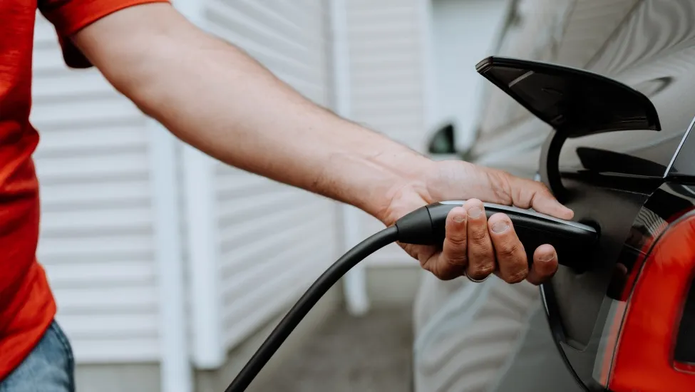 Close-up of a person's arm and hand as they charge an electric vehicle.