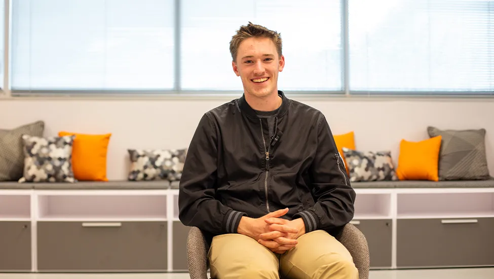 Wesley Pitts smiles at the camera while seated on a gray couch