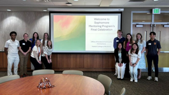 UT Haslam Sophomore Mentoring Program participants pose next to a screen showing the name of their program