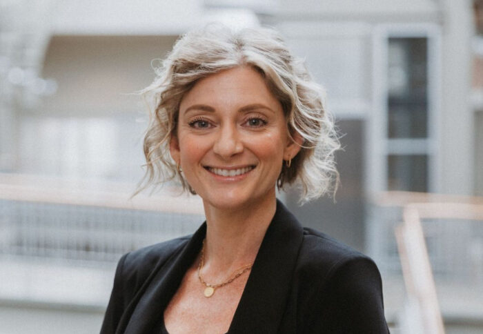Sara Easler, in a black dress jacket and blouse. poses in the Haslam Business Building Atrium.