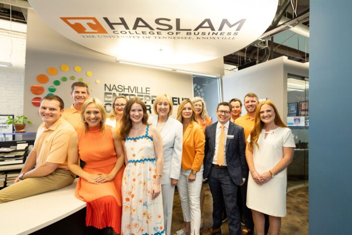 A group of NEC employees pose with UT Chancellor Donde Plowman, center, and Haslam's Deborah Watts, on Plowman's left, under the new cloud painting bearing Haslam's logo in the NEC reception area.
