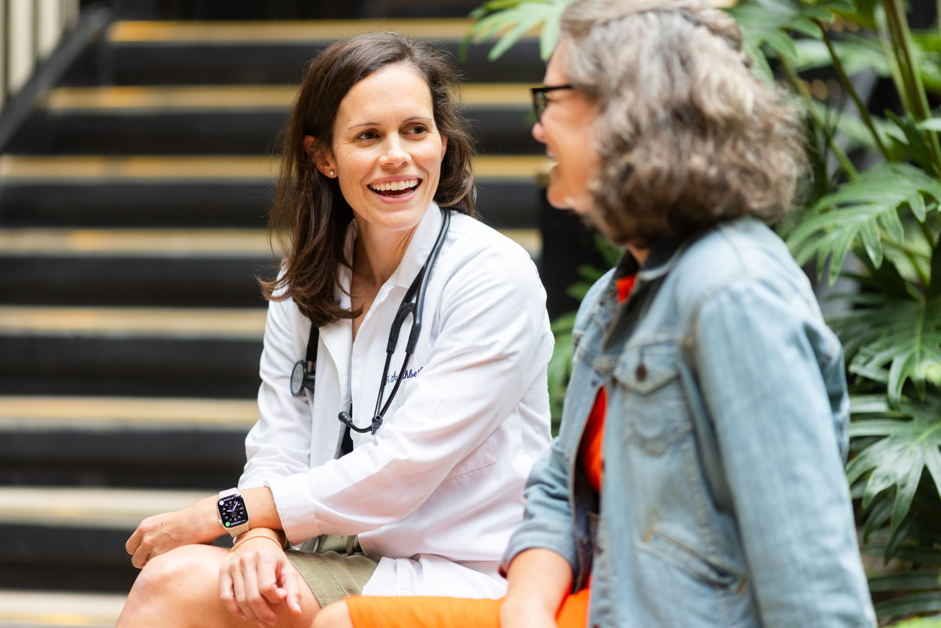 A female doctor wears a stethoscope and white while speaking to a female patient.