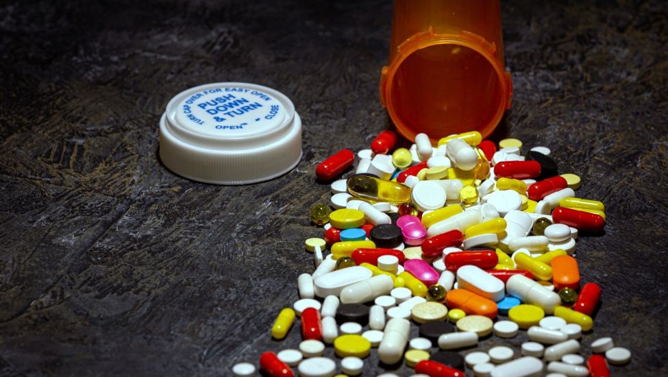 An assorted of pills has spilled on a dark surface from an overturned prescription bottle