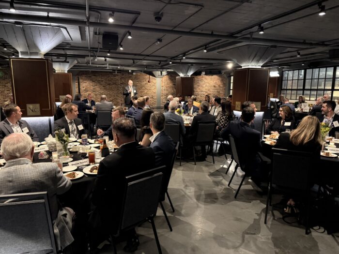 Boyd Center director Don Bruce holds a microphone and presents survey data at the Tennessee Business Leaders Dinner, a dinner with about 62 business leaders seated at tables around the room. 