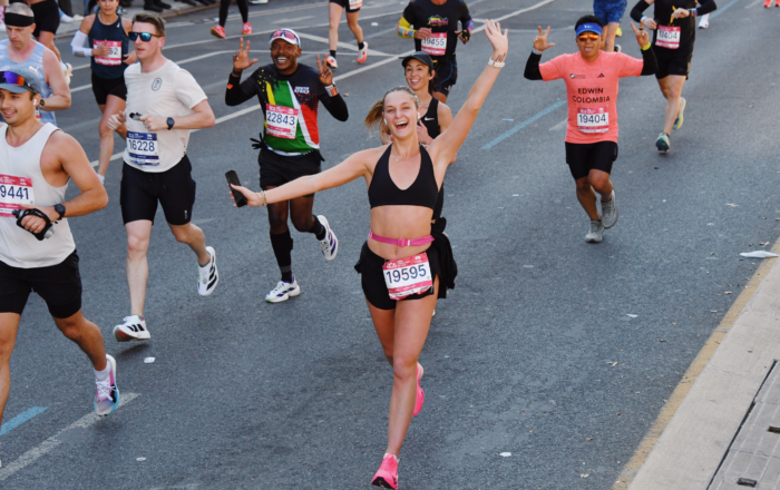Alyssa Drendel running a marathon with her hands in the air smiling at the camera.