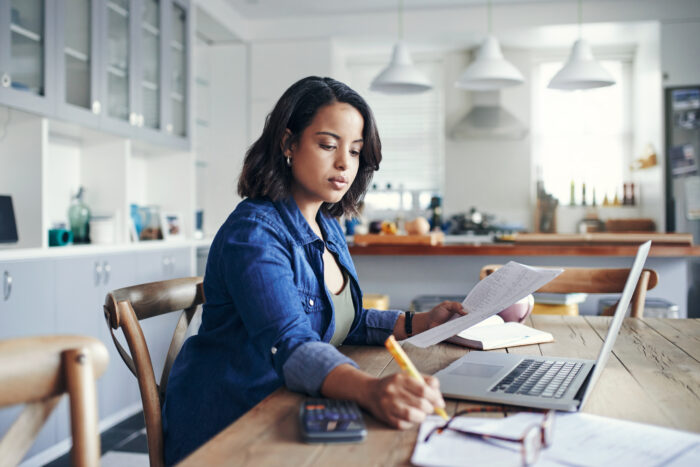 A young woman using a laptop and going through paperwork to budget.