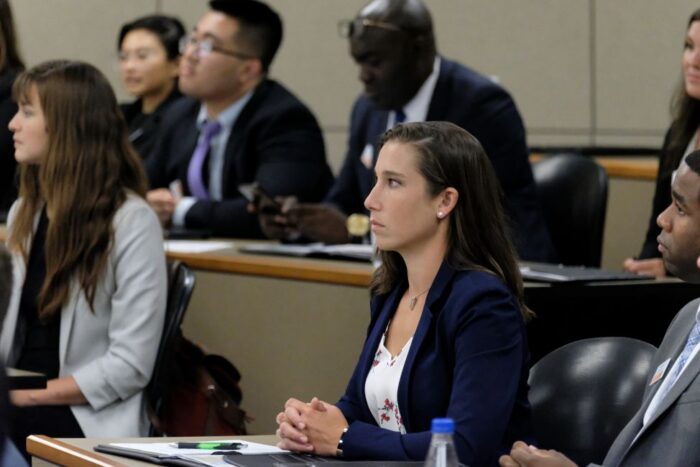UT graduate business students in professional attire listen to a lecture in a lecture hall.